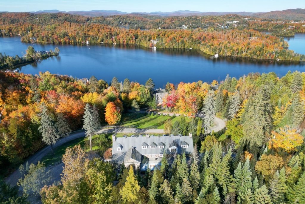 Vue aérienne du Manoir Davis à Sainte-Agathe-des-Monts entouré des forêts colorées des Laurentides, bordant un grand lac paisible en automne.
